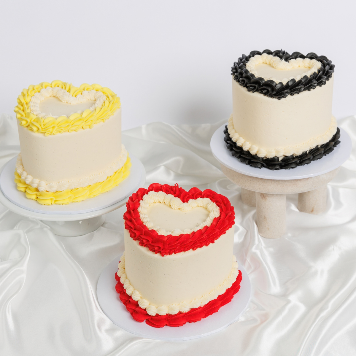 Three white Vintage Heart Cakes with yellow, black and red buttercream trim by The Cupcake Queens