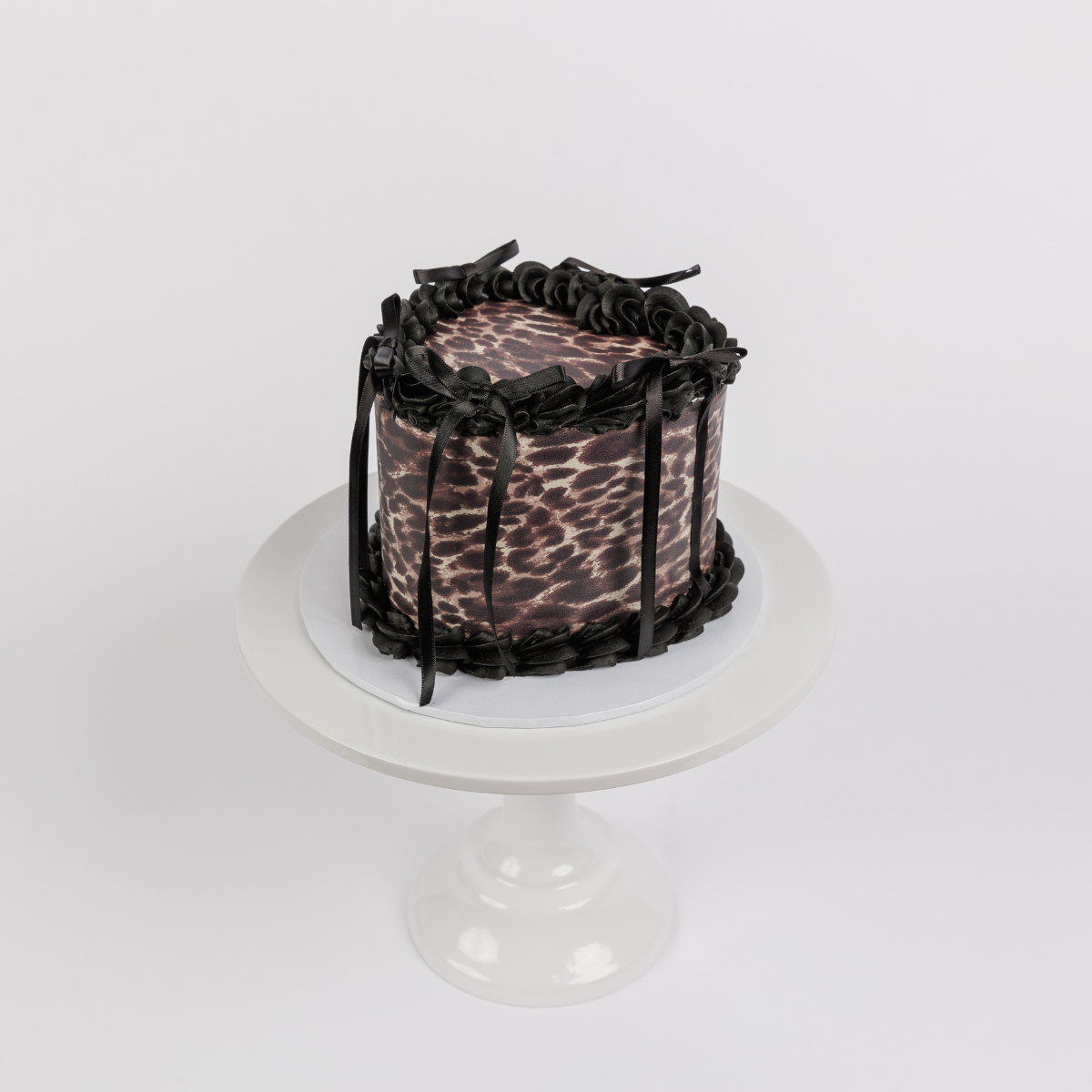 Leopard Print Vintage Heart Cake with black buttercream piping and black ribbons on a white cake stand, side view