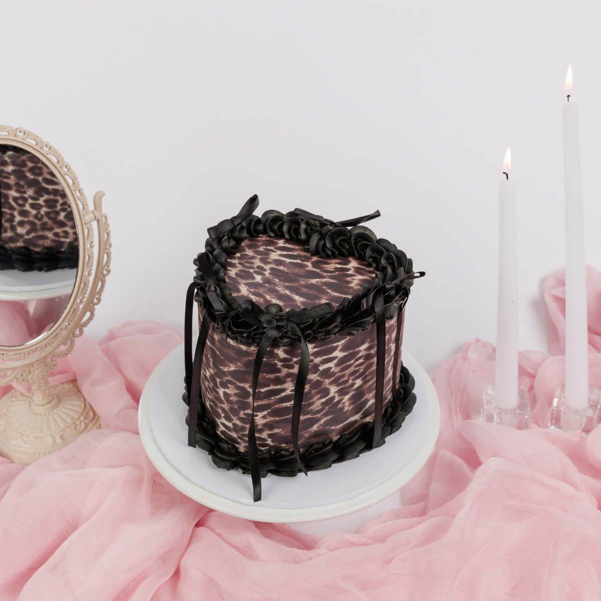 Leopard Print Vintage Heart Cake with black buttercream piping and black ribbons on a white cake stand, side view